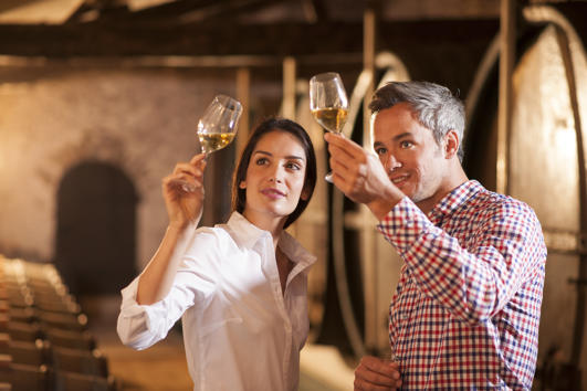 Couple tasting a glass of white wine in a traditional cellar surrounded by wooden barrels.